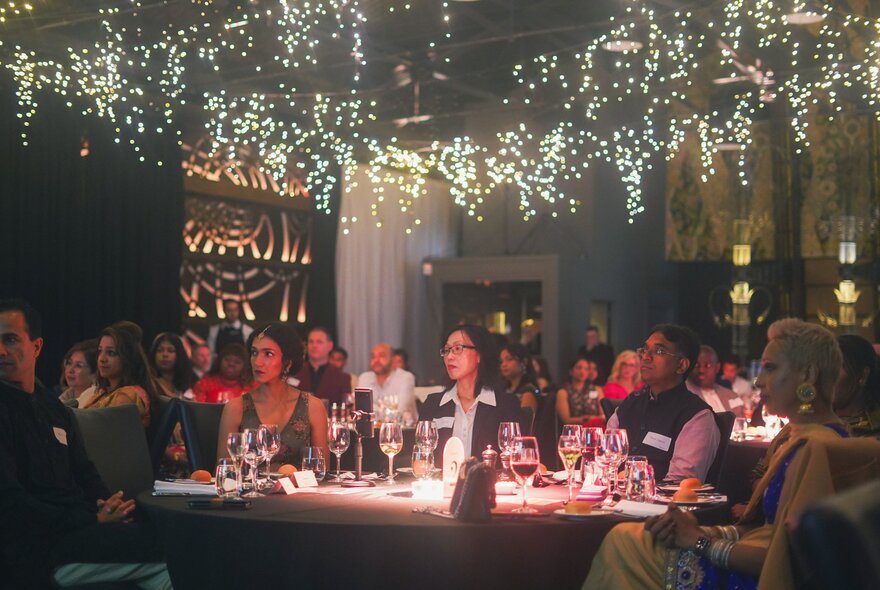 People seated at a banquet table in a funtion room with fairy lights across the ceiling.