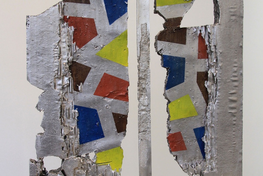 An abstract silver artwork with squares of red, blue and yellow arranged on it.