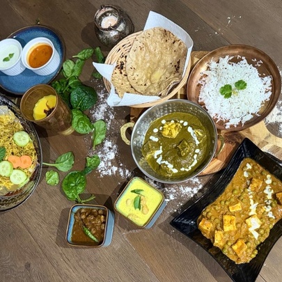 Looking directly down on a table filled with various Indian dishes, naan, rice and drinks. 