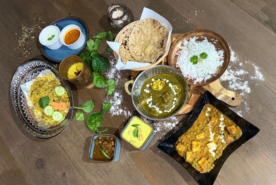 Looking directly down on a table filled with various Indian dishes, naan, rice and drinks. 