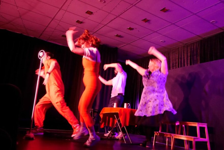 Four actors on stage performing an improvised theatre routine, all of them waving their arms above their heads.