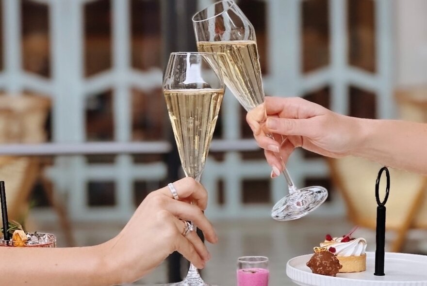 Two hands bringing two glasses of champagne together in a clinking glasses toasting motion.