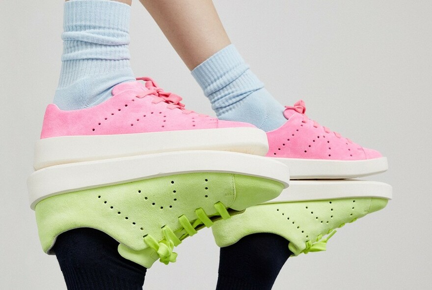 Models legs wearing blue socks and pink sneakers with deep white sole, standing on black legs wearing pale green sneakers.