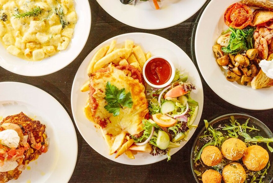 An array of white plates with dishes including gnocchi and arancini.