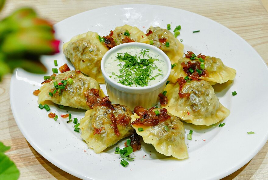 A plate of pierogi with a bowl of sour cream. 