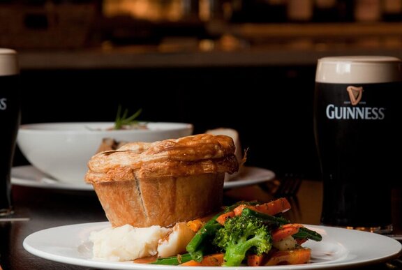 A pie one a plate with veggies and a pint of Guinness. 