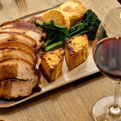 Roast pork platter with baked vegetables and glass of red wine.