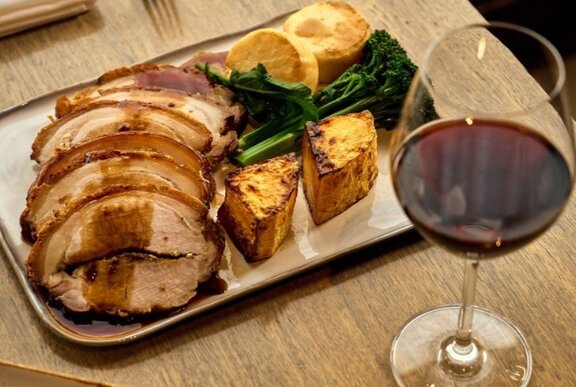 Roast pork platter with baked vegetables and glass of red wine.