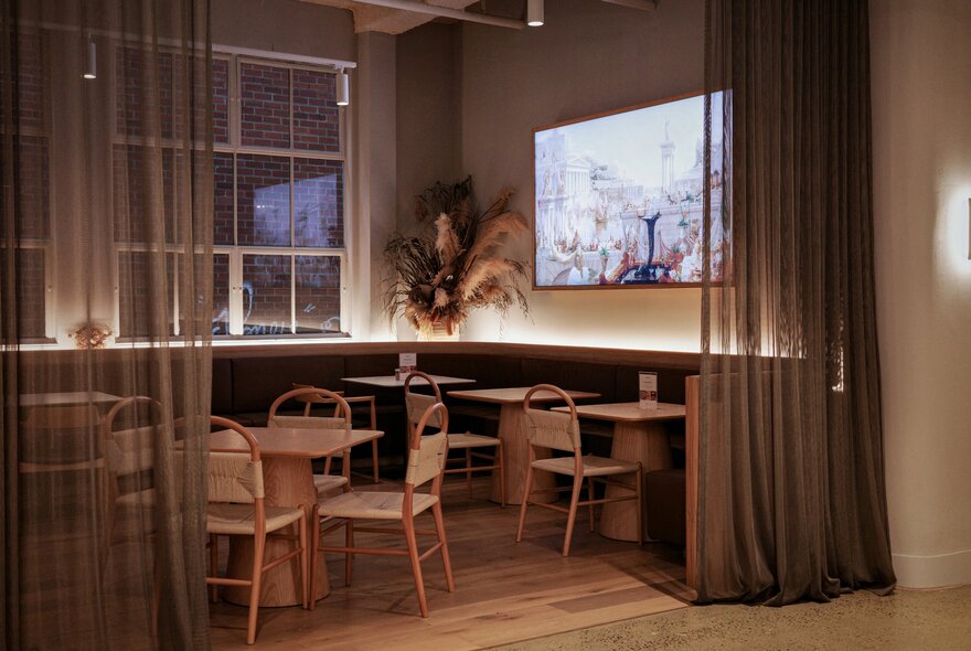 Light-filled interior of Soaz 22 cafe, with pale blonde wood tables and chairs, sheer curtains creating a semi private area of tables and chairs in a corner.