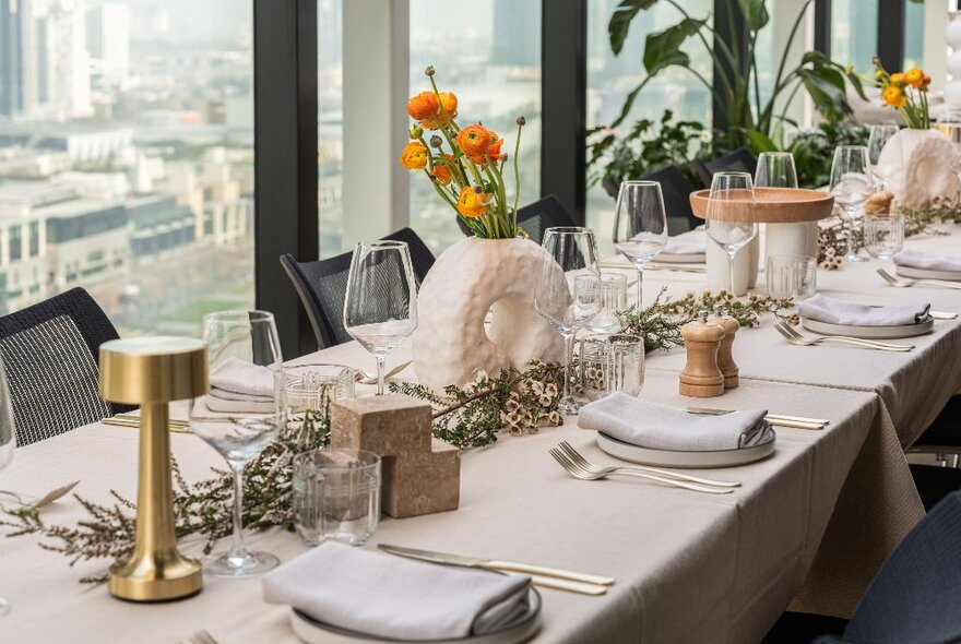 A long table in front of a window, set with plates, cutlery, napkins and christmas themed decorations and flowers.