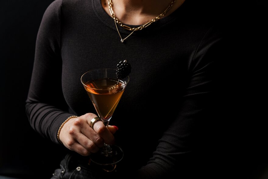 A woman wearing black holding a cocktail.