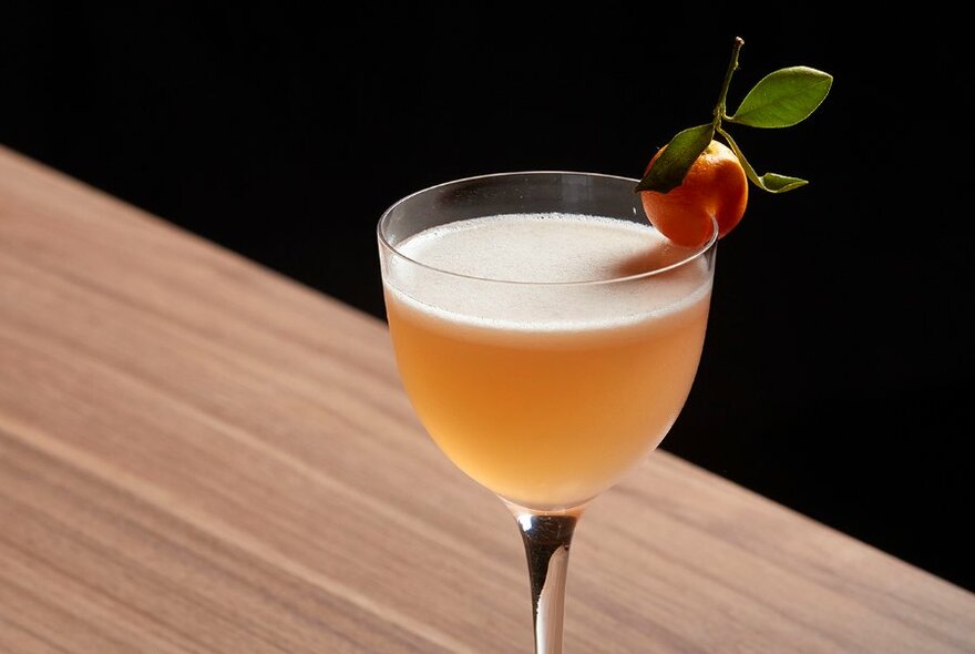 Amber coloured cocktail in a small glass with a cumquat garnish.