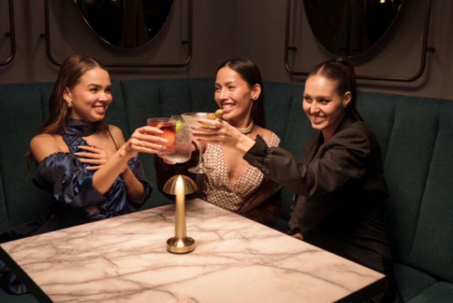 Three friends enjoying cocktails in a booth seating area with a marble table.