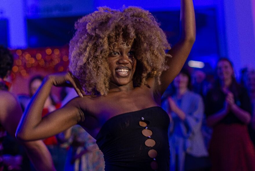 A woman with big hair dancing while people looking on clap in a nightclub. 