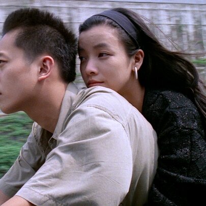 A still image from a Korean film showing a woman holding on to a man on a motorcycle.