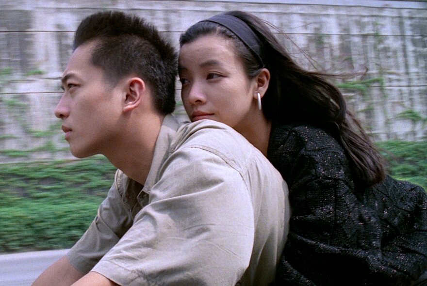A still image from a Korean film showing a woman holding on to a man on a motorcycle.