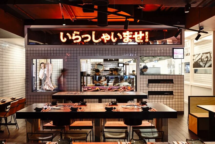 Japanese restaurant interior with cooking station and long shared table with seating.