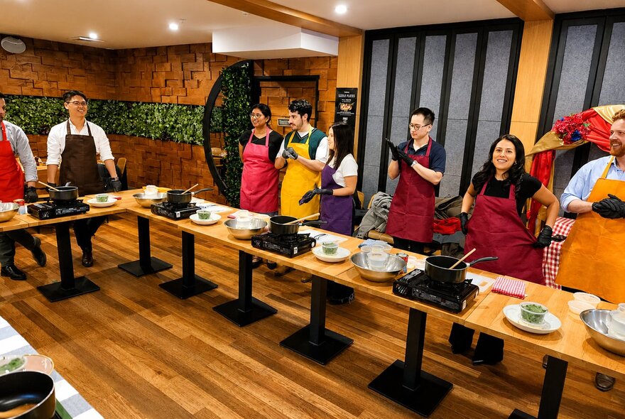 Cooking workshop participants wearing black gloves while working at stovetop workbenches in a U-shaped arrangement.