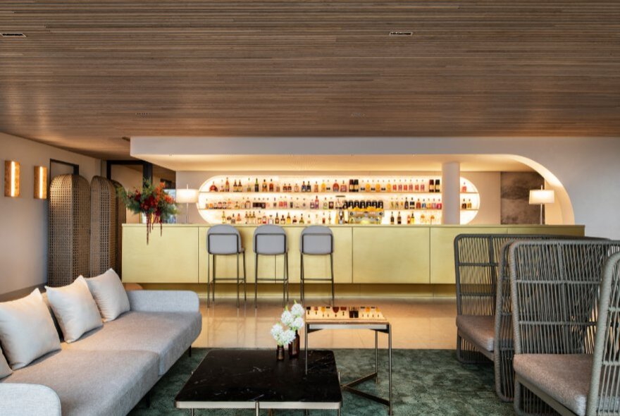 The minimalist interior of a modern restaurant with a wood-lined ceiling and yellow-fronted bar.