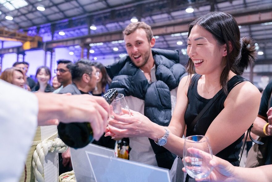 People smiling while having sake poured into glasses they are holding out to a stall\ holder at the Sake Festival.