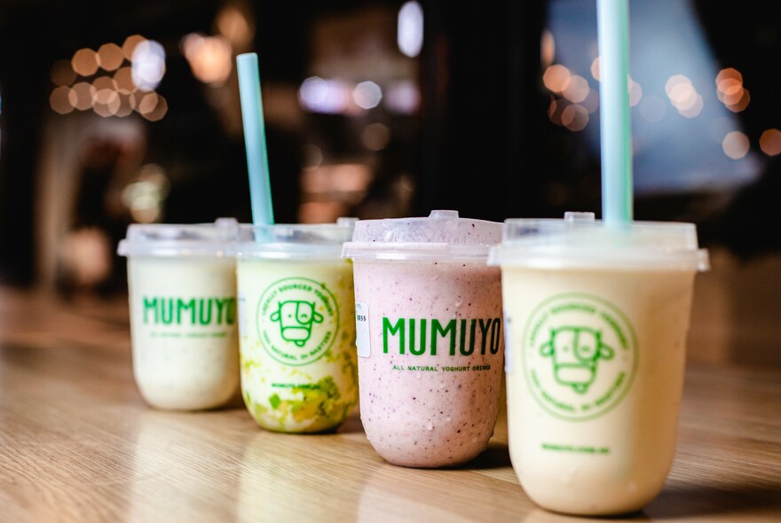 Several flavoured yoghurt drinks in takeaway containers with plastic straws.