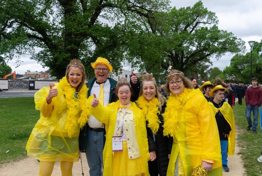 A race team wearing yellow standing in a park under trees.