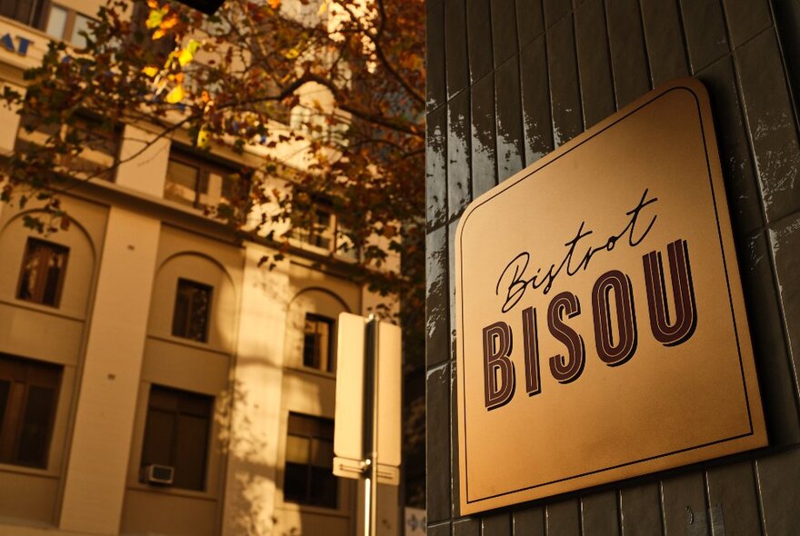 The sign at the front of Bistrot Bisou with old city buildings visible in the background