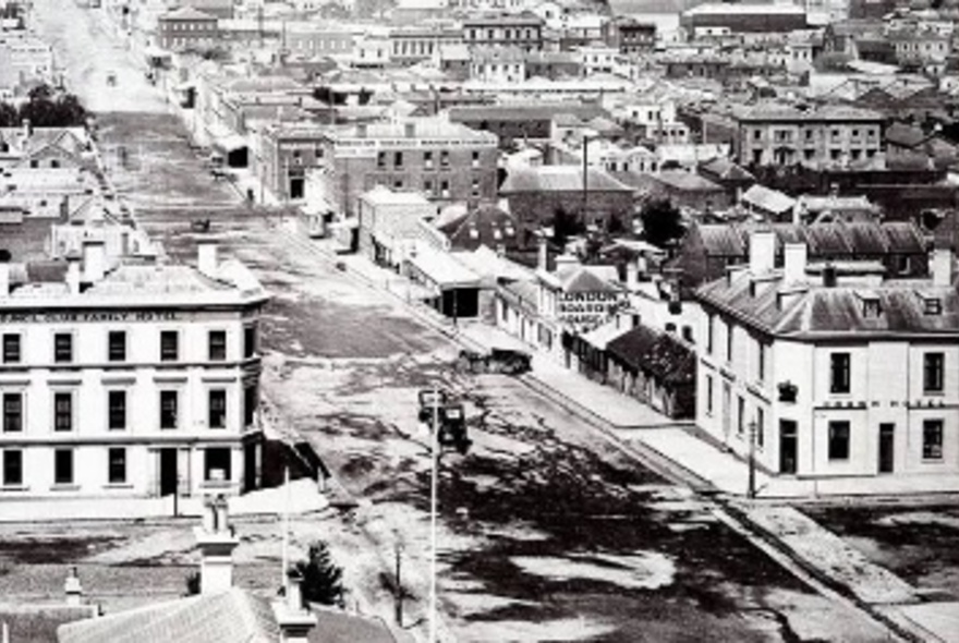 Victorian-era view of Melbourne taken from a high vantage point, looking down a wide dirt road lined with colonial-era buildings.