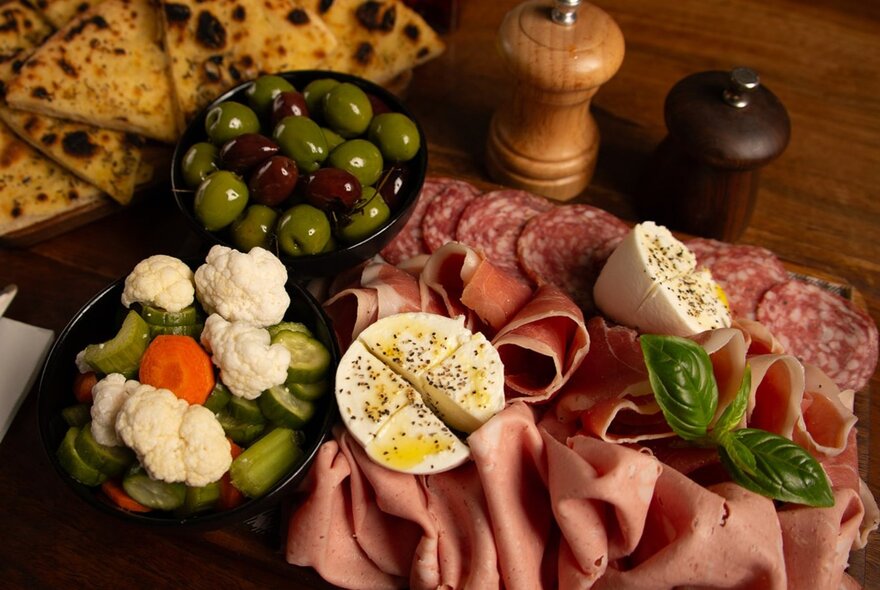 Antipasto platter with mortadella, olives and pepper and salt mills. 