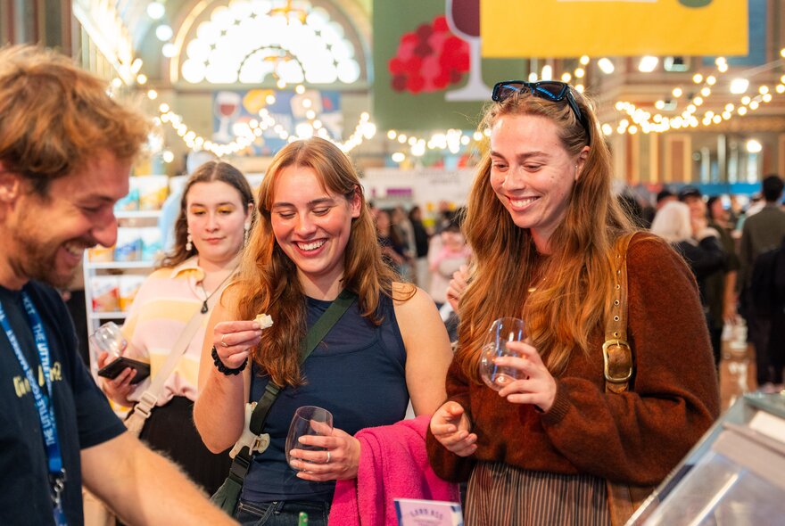 Visitors smiling and enjoying food and drink tastings at The Little Food Market, an artisanal food and wine event held at the Royal Exhibition Building.