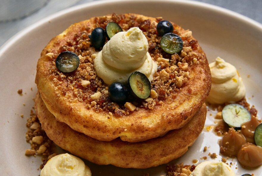 Two breakfast crumpets on a white plate, decorated with fresh berries, chopped nuts and cream.