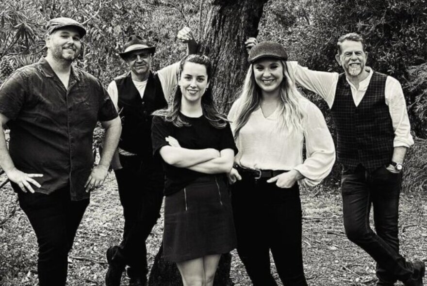 Irish band standing under trees in a park setting, wearing caps.