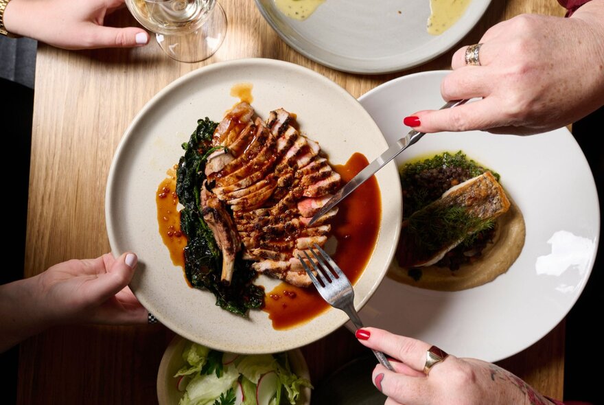 A pair of hands passing a plate of food to someone across a dining table.