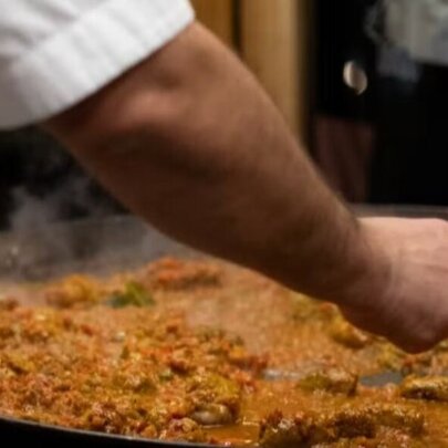 A hand stirring a large pan of paella.