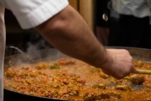 A hand stirring a large pan of paella.