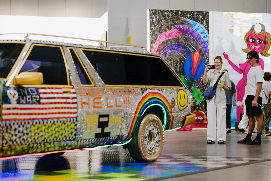 People loking at a station wagon decorated with artwork in a gallery space.