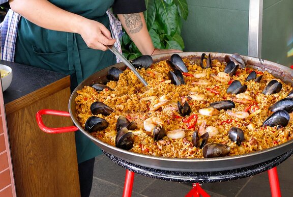 A chef preparing a bowl of seafood paella from a large pan.