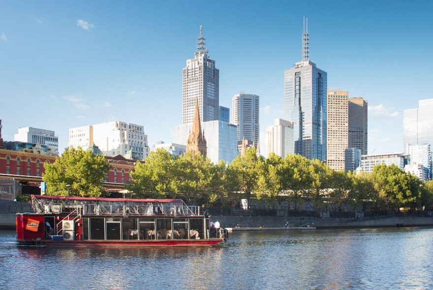 A boat cruising down the Yarra River with the city skyline in view.