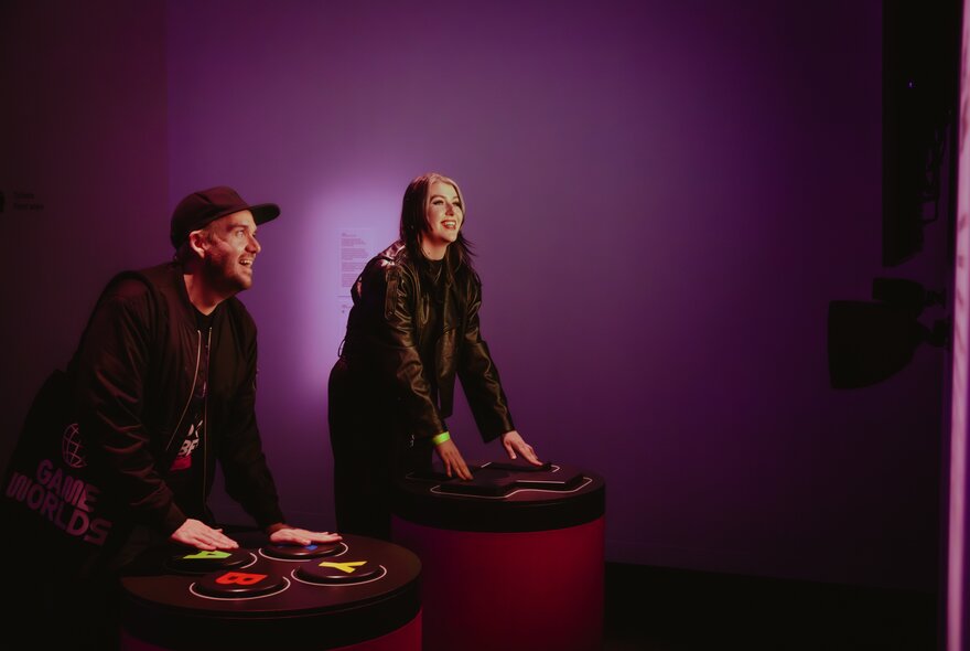 People playing games stations in a purple-lit dark room.
