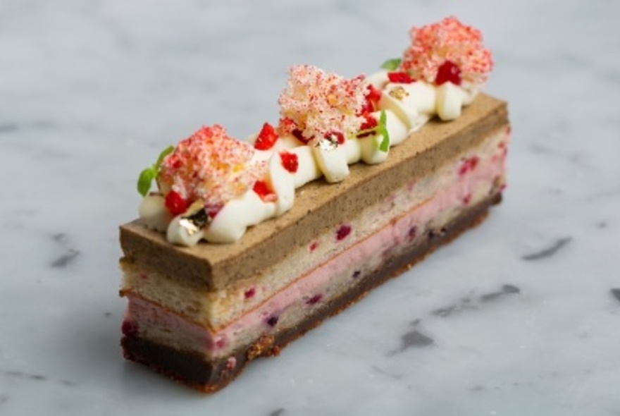 A thin multi-layered dessert slice, topped with cream, and delicately coloured sweet garnishes.