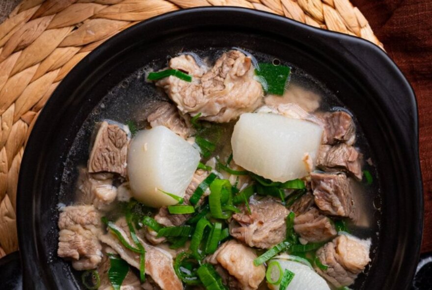 Bowl of meat and onions on a straw mat.