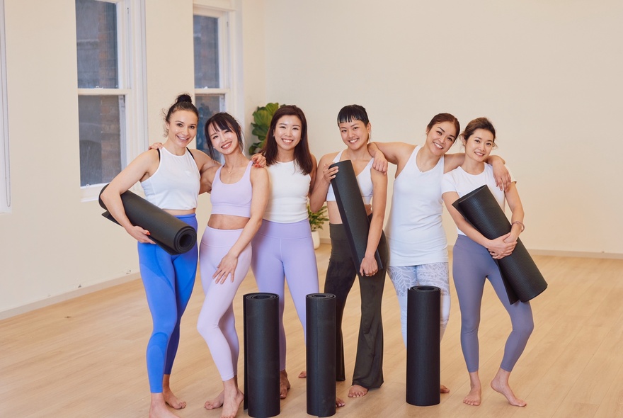 Group of yoga participants wearing exercise wear and holding yoga mats.