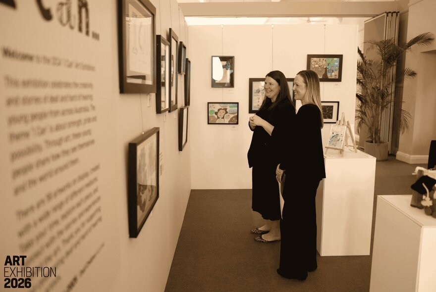 Sepia-toned image of two women viewing art on a gallery wall. 