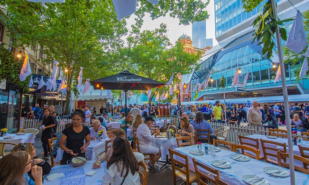 People dining at tables at a street festival.