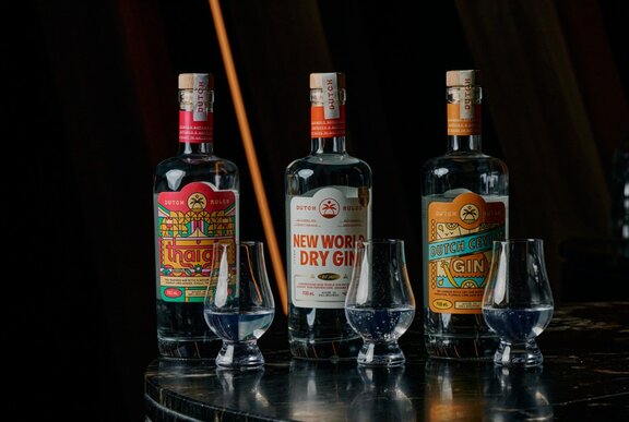 Three gin bottles and three glasses, displayed on a black surface with a black background.