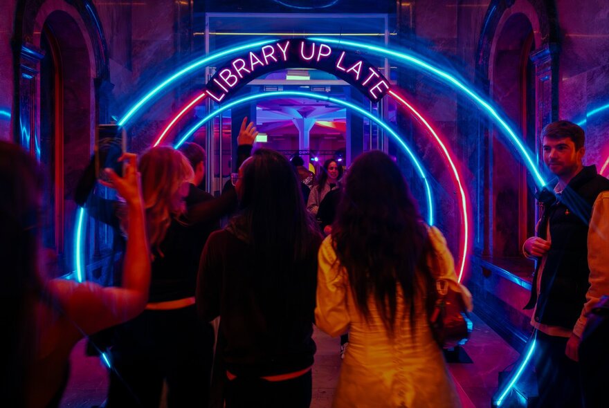 People walking through tunnel-like neon lights into State Library Victoria.
