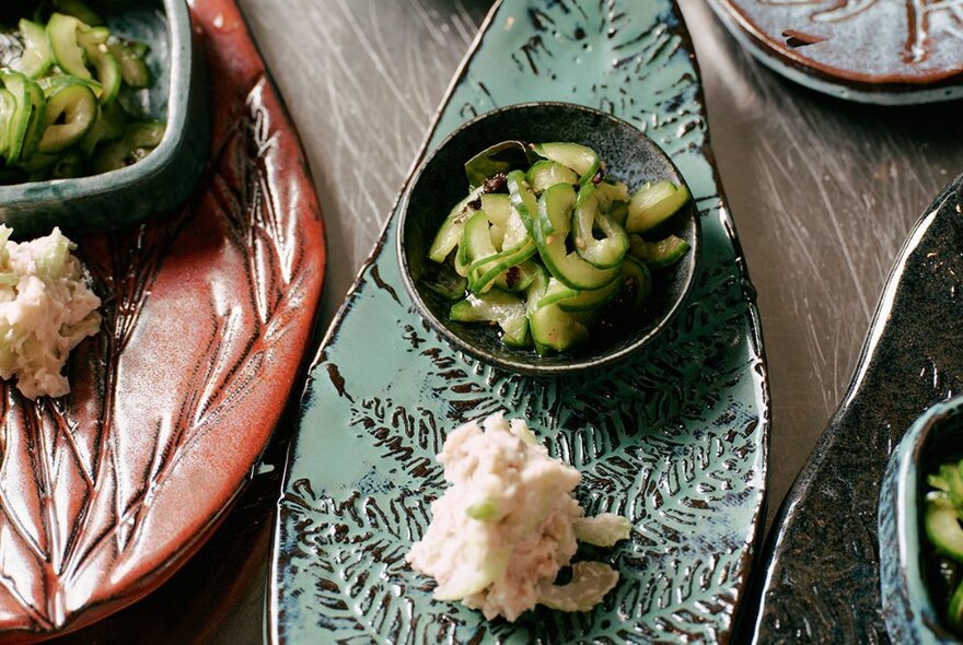 Bowls and scoops of condiments on brown and green ceramic plates. 