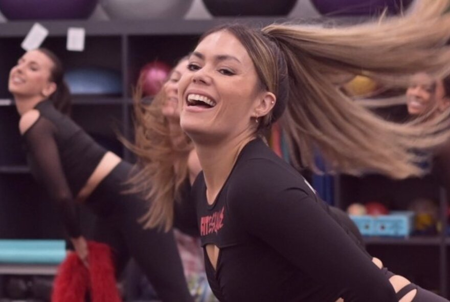 Women using burlesque stances in an exercise class, hair flying, bending on one hip with feather boas.