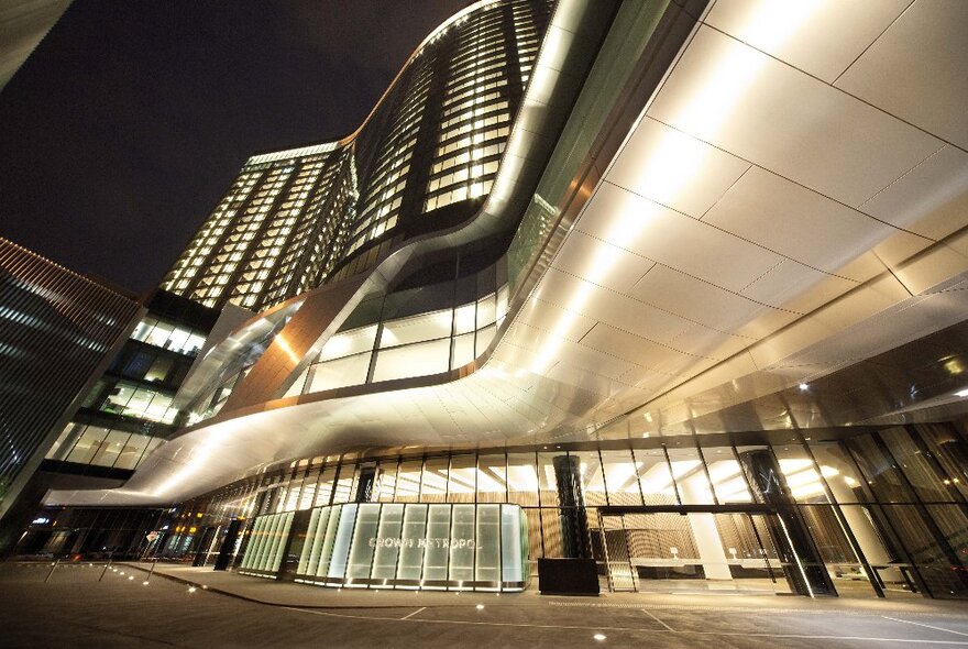 Hotel exterior with curved metal design and multiple windows, lit up at night.