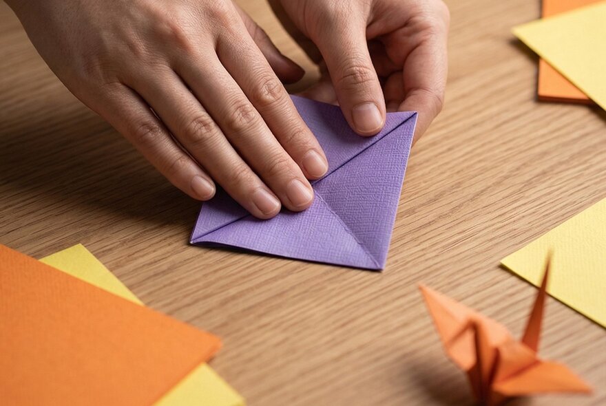 Hands folding coloured paper square to make origami.